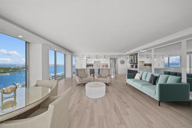 living room with light wood-type flooring, a water view, and a wall of windows