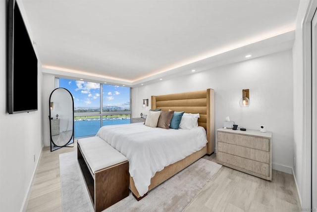 bedroom featuring a water view, light wood-type flooring, a wall of windows, and access to outside