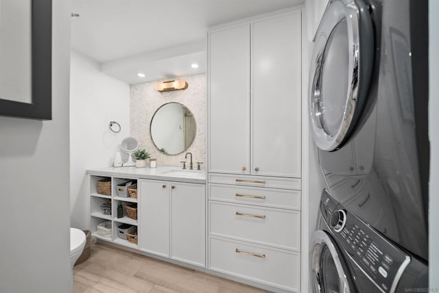 laundry room with sink, stacked washing maching and dryer, and light hardwood / wood-style flooring