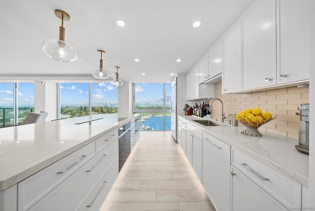 kitchen featuring pendant lighting, white cabinets, sink, tasteful backsplash, and light stone counters