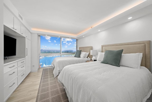 bedroom with expansive windows, light hardwood / wood-style floors, and a water view