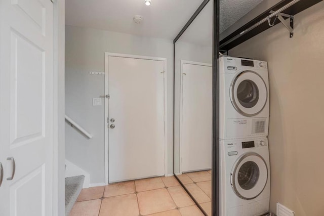 clothes washing area featuring stacked washer / dryer, light tile patterned floors, and a textured ceiling