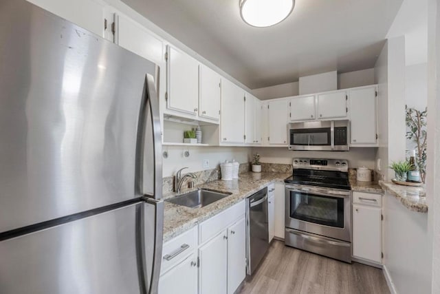 kitchen with sink, white cabinetry, light stone counters, light wood-type flooring, and appliances with stainless steel finishes