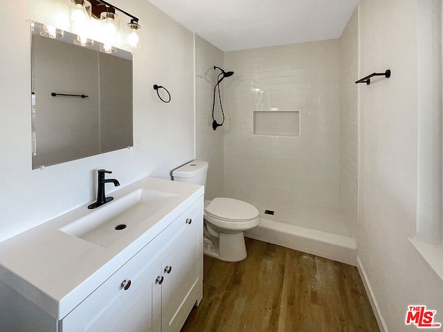 bathroom featuring a tile shower, vanity, wood-type flooring, and toilet