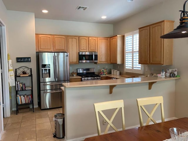 kitchen featuring light tile patterned flooring, a breakfast bar area, appliances with stainless steel finishes, and kitchen peninsula