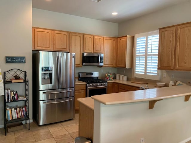 kitchen with a breakfast bar area, light tile patterned floors, kitchen peninsula, and stainless steel appliances