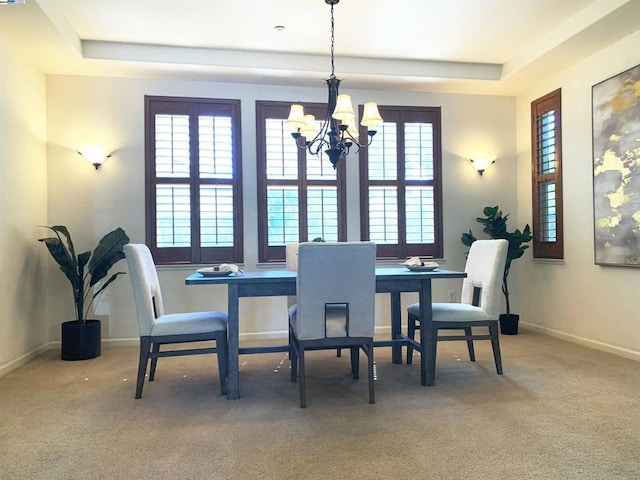 carpeted dining space featuring a healthy amount of sunlight, a tray ceiling, and a chandelier