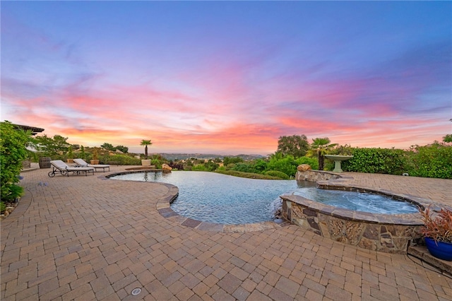 pool at dusk with an in ground hot tub, pool water feature, and a patio