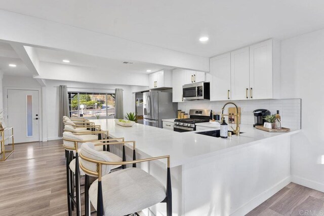 kitchen featuring kitchen peninsula, appliances with stainless steel finishes, backsplash, sink, and white cabinets