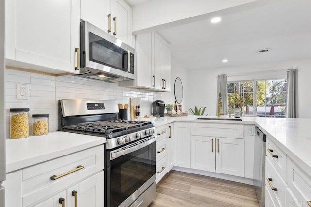 kitchen with light wood-style flooring, appliances with stainless steel finishes, light countertops, white cabinetry, and backsplash