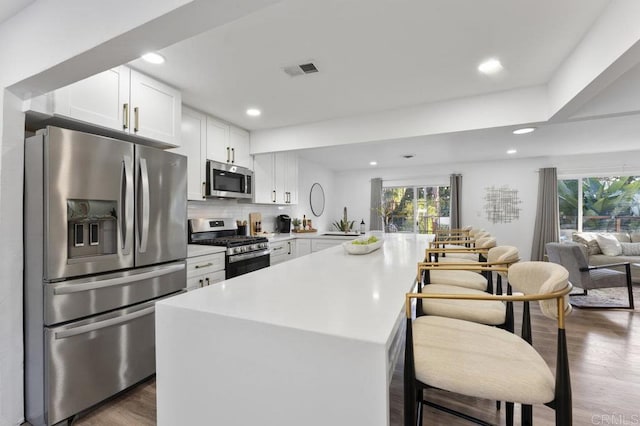 kitchen with visible vents, appliances with stainless steel finishes, open floor plan, white cabinetry, and wood finished floors