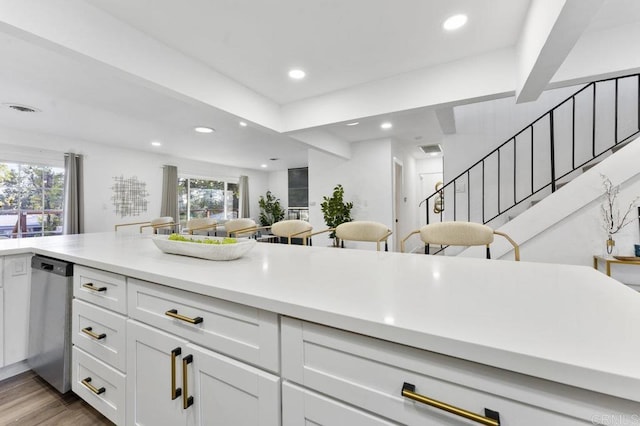 kitchen featuring white cabinets, wood finished floors, light countertops, a healthy amount of sunlight, and stainless steel dishwasher