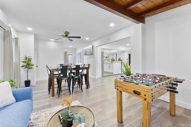 recreation room featuring ceiling fan, recessed lighting, baseboards, light wood finished floors, and beamed ceiling