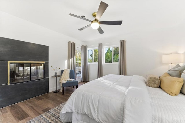 bedroom with wood finished floors, a multi sided fireplace, a ceiling fan, and baseboards