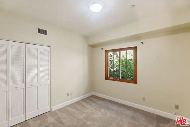 unfurnished bedroom with light colored carpet and a closet