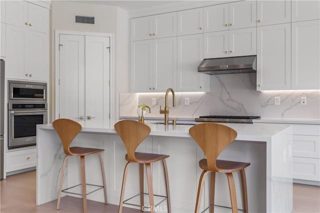 kitchen with a kitchen breakfast bar, white cabinets, light wood-type flooring, and appliances with stainless steel finishes