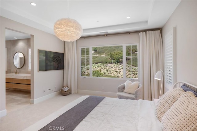 carpeted bedroom with a tray ceiling and ensuite bath