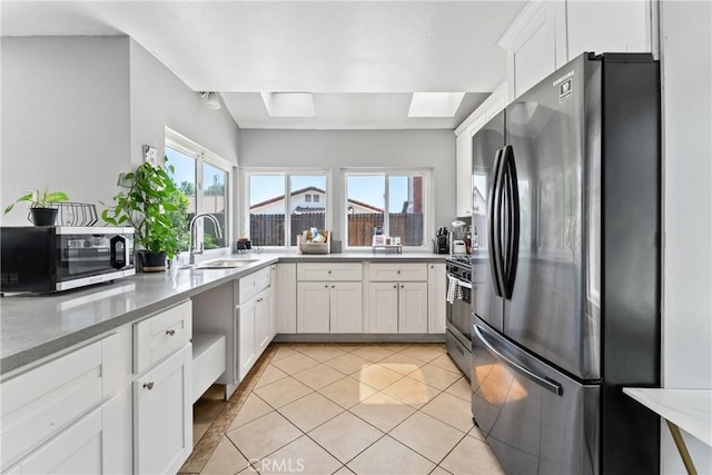 kitchen featuring a skylight, appliances with stainless steel finishes, light stone counters, white cabinetry, and a sink