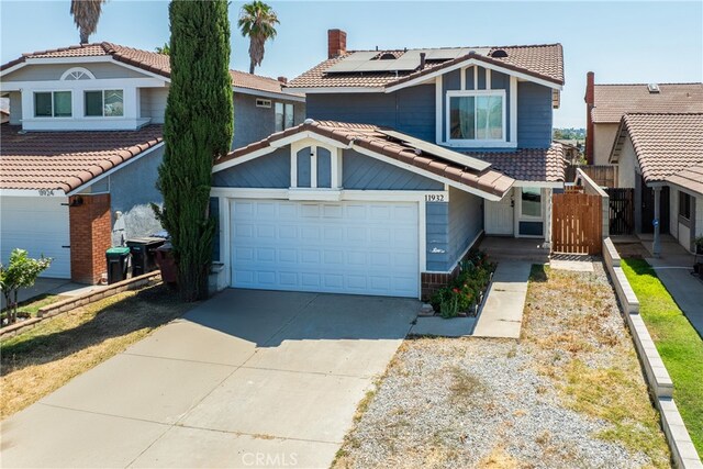 view of front of house featuring a garage, fence, driveway, a tiled roof, and roof mounted solar panels