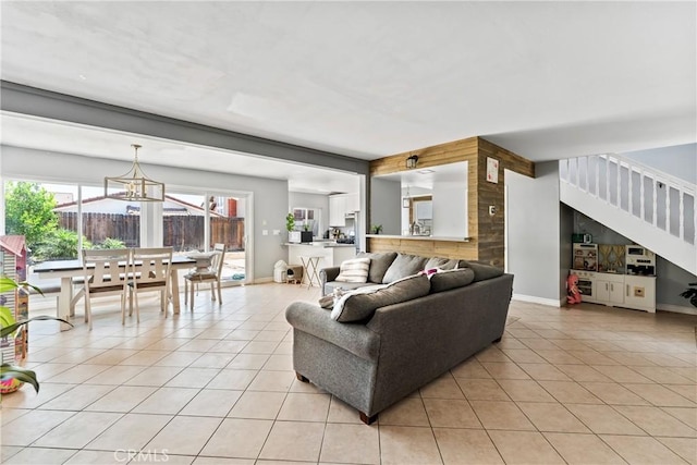 living area featuring stairs, a notable chandelier, baseboards, and light tile patterned floors