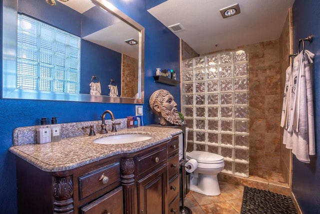 bathroom featuring toilet, a tile shower, vanity, and tile patterned floors