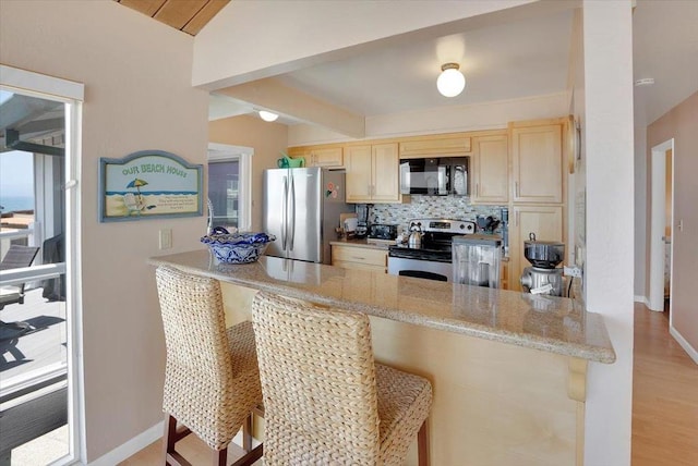 kitchen with appliances with stainless steel finishes, a kitchen bar, light wood-type flooring, kitchen peninsula, and decorative backsplash