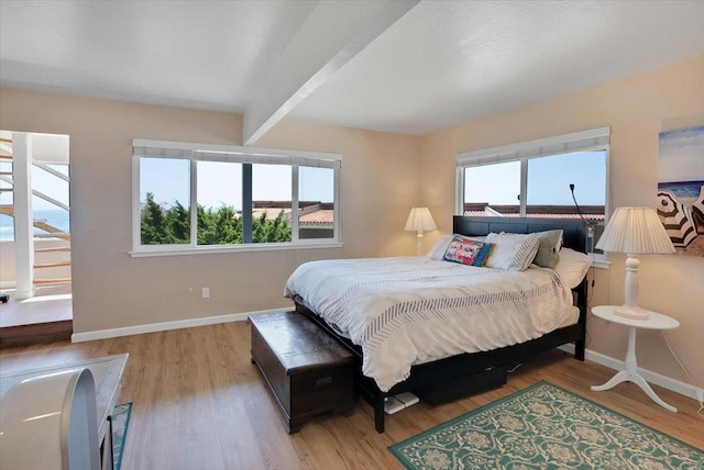 bedroom featuring beamed ceiling, light hardwood / wood-style flooring, and multiple windows