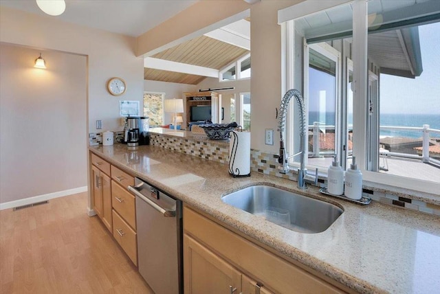 kitchen with light stone countertops, sink, vaulted ceiling with beams, light hardwood / wood-style floors, and stainless steel dishwasher