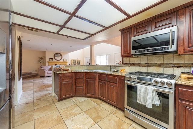 kitchen with light tile patterned floors, kitchen peninsula, stainless steel appliances, light stone countertops, and decorative backsplash