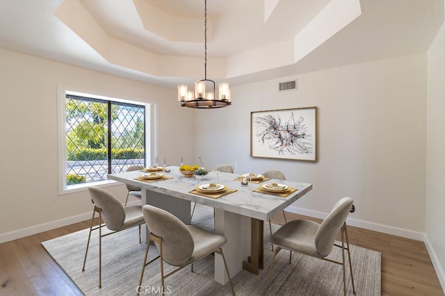 dining area featuring a notable chandelier, a tray ceiling, and light wood-type flooring