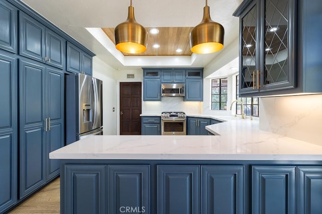 kitchen featuring appliances with stainless steel finishes, decorative light fixtures, decorative backsplash, a raised ceiling, and blue cabinetry