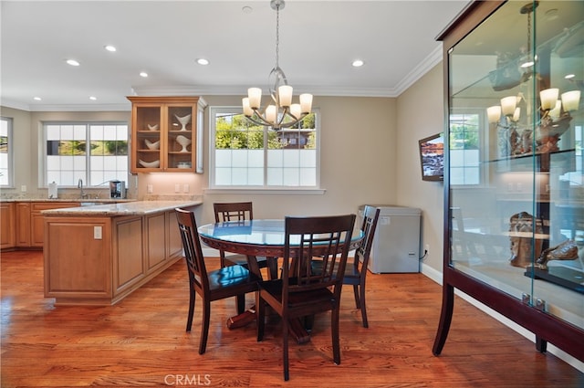 dining area featuring sink, light hardwood / wood-style floors, ornamental molding, and an inviting chandelier