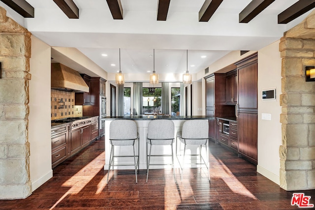 kitchen featuring hanging light fixtures, a kitchen island with sink, wall chimney range hood, dark hardwood / wood-style flooring, and decorative backsplash