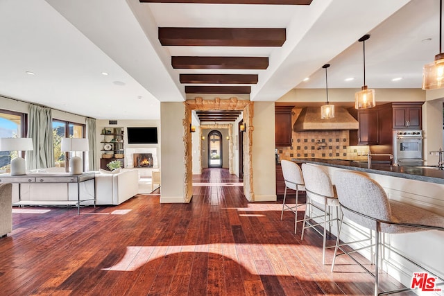 kitchen featuring pendant lighting, beamed ceiling, wall chimney exhaust hood, dark hardwood / wood-style floors, and a kitchen bar