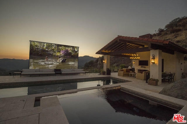 pool at dusk featuring an outdoor hangout area, a mountain view, a patio area, and a gazebo