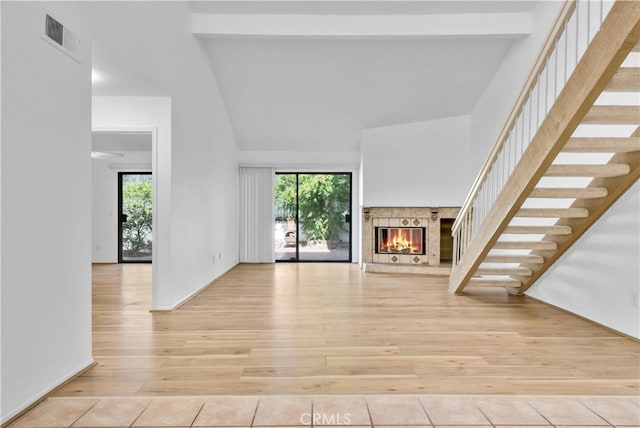 unfurnished living room with a fireplace, beam ceiling, high vaulted ceiling, and light hardwood / wood-style flooring