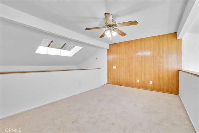 carpeted empty room with vaulted ceiling with skylight, wooden walls, and ceiling fan