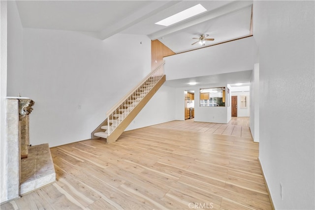 unfurnished living room with light hardwood / wood-style floors, lofted ceiling with skylight, and ceiling fan