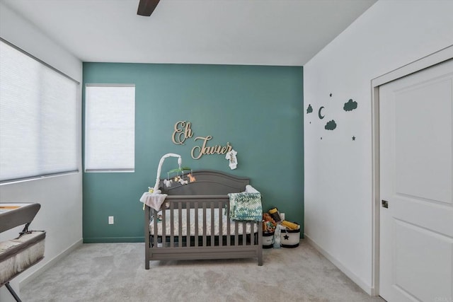 bedroom featuring ceiling fan, a crib, and light carpet