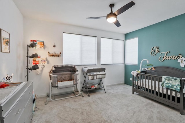 carpeted bedroom with ceiling fan and a nursery area