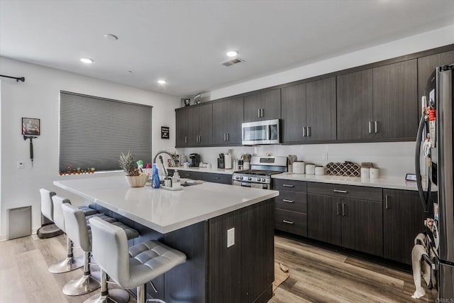 kitchen featuring appliances with stainless steel finishes, sink, a center island with sink, light hardwood / wood-style floors, and a breakfast bar area