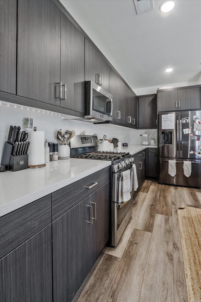 kitchen with appliances with stainless steel finishes, dark brown cabinetry, and light hardwood / wood-style floors