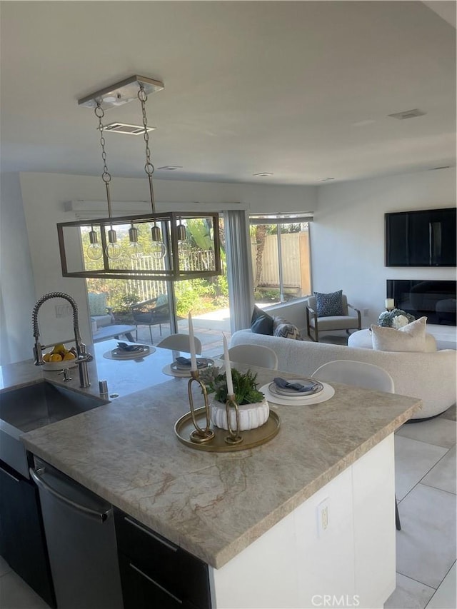 kitchen featuring stainless steel dishwasher, sink, light tile patterned floors, a center island, and hanging light fixtures