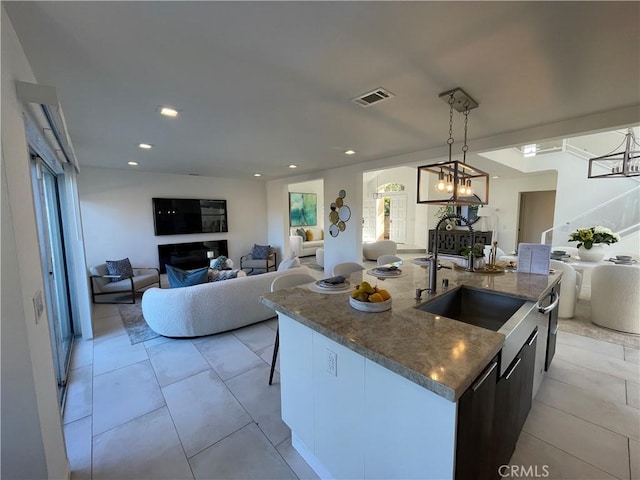 kitchen with light tile patterned flooring, an inviting chandelier, hanging light fixtures, and an island with sink