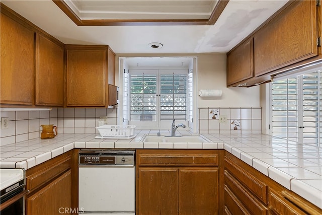 kitchen featuring tile counters, white dishwasher, sink, range, and tasteful backsplash