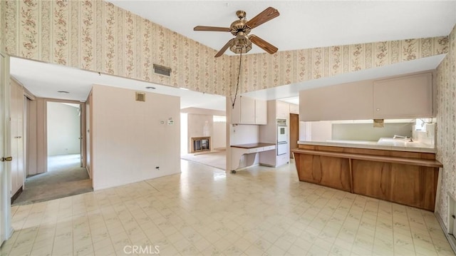 kitchen with double oven, kitchen peninsula, and ceiling fan