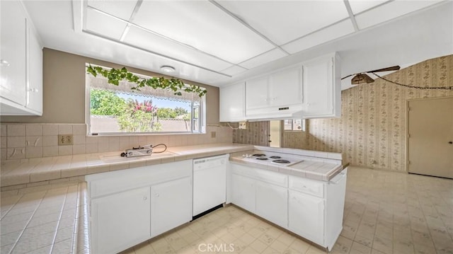 kitchen with tile counters, sink, kitchen peninsula, white appliances, and white cabinets