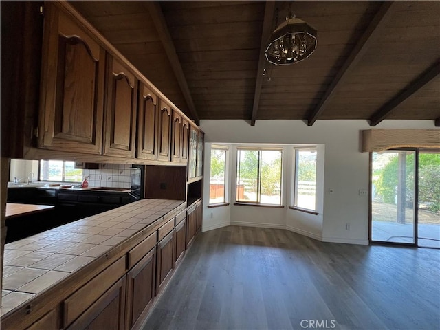 kitchen featuring vaulted ceiling with beams, tile counters, wood-type flooring, and a wealth of natural light