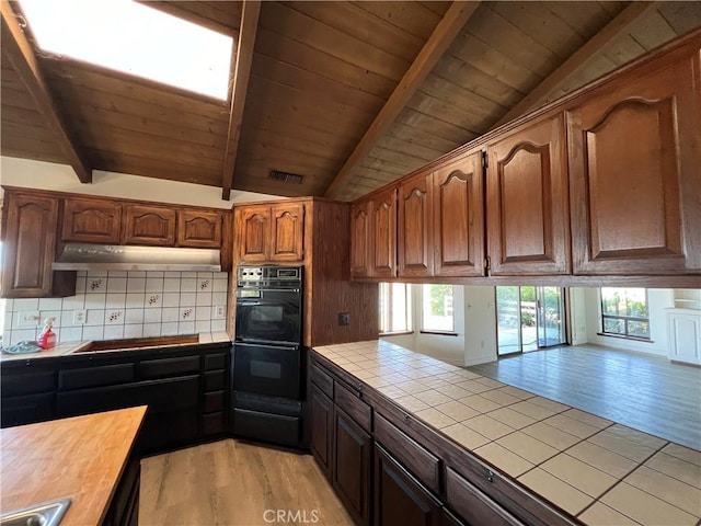 kitchen featuring lofted ceiling with beams, light hardwood / wood-style floors, tile counters, and black appliances