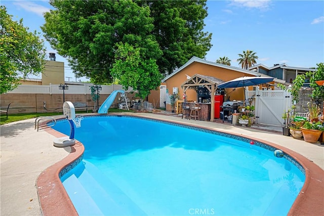 view of swimming pool with a bar, a patio, and a water slide